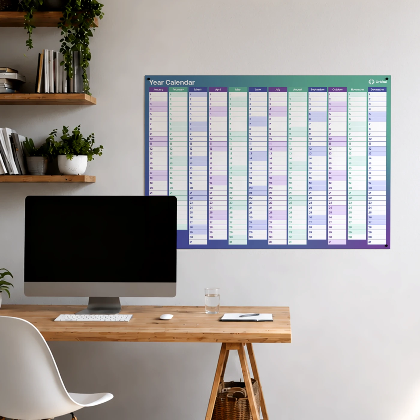 A large, teal and purple annual Wall Planner hanging in a home office setup above a wooden desk with a computer monitor.