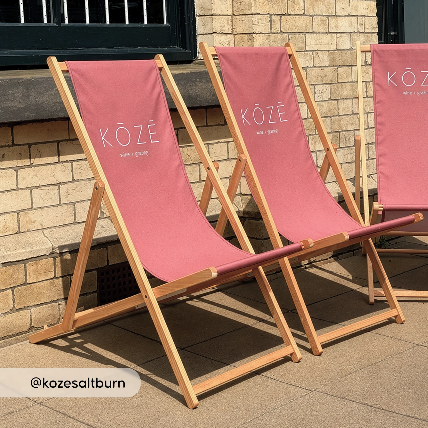 Three pink KOZE deck chairs arranged outside against a brick wall