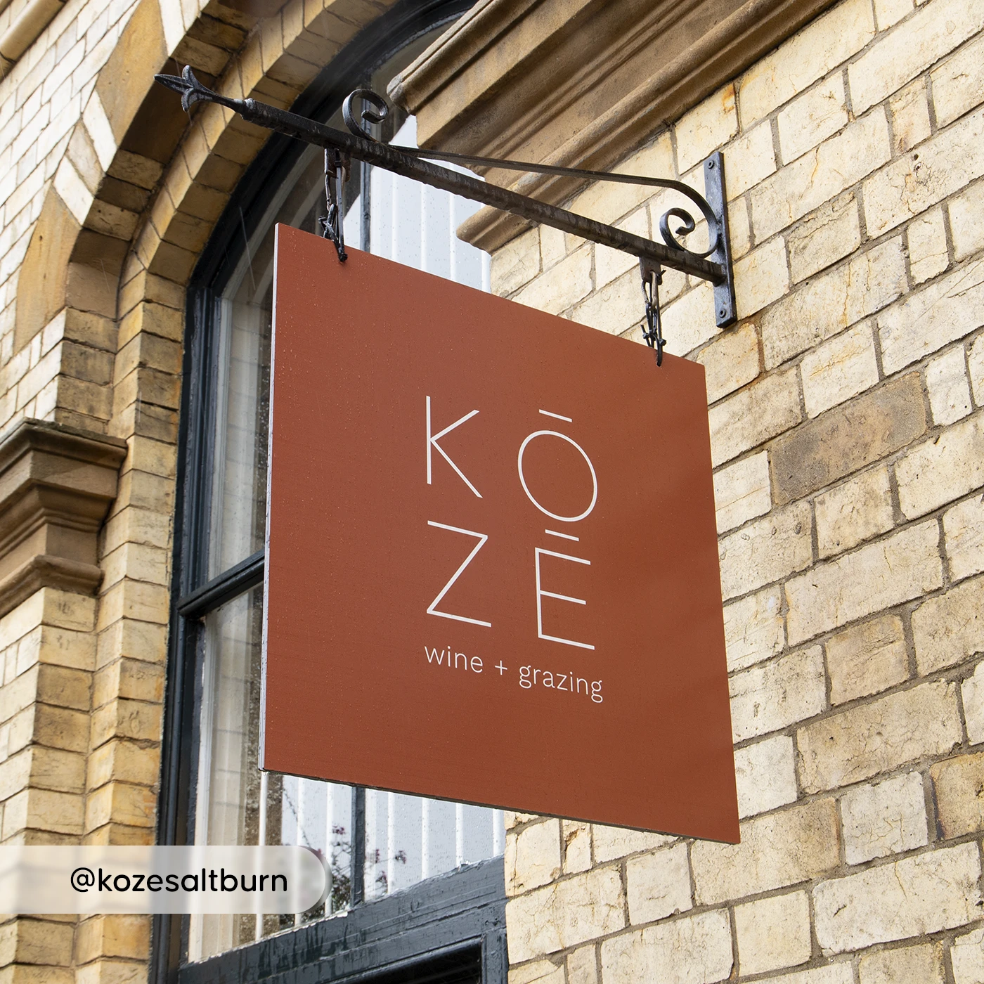 KOZE dibond sign mounted on a metal bracket against a brick wall