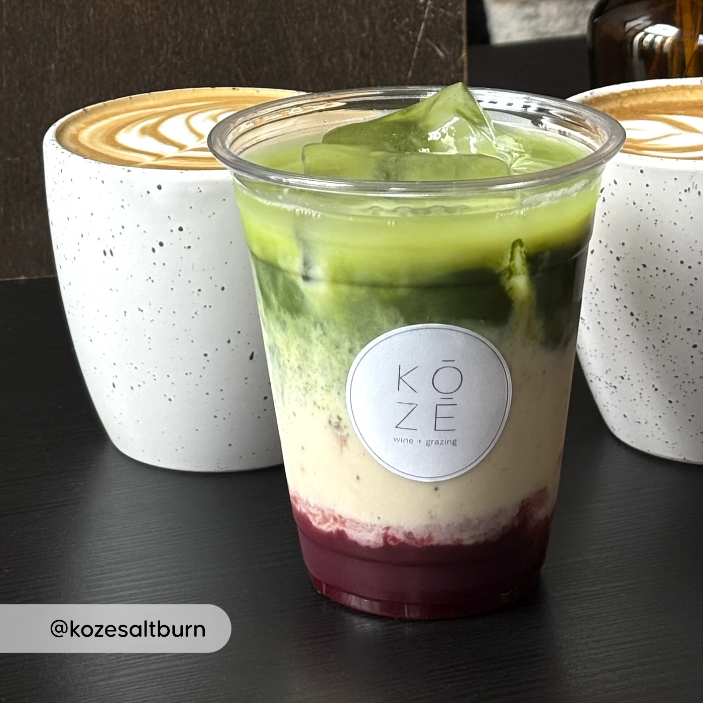 Close‑up of KOZE round sticker on a layered matcha iced drink with two lattes in the background