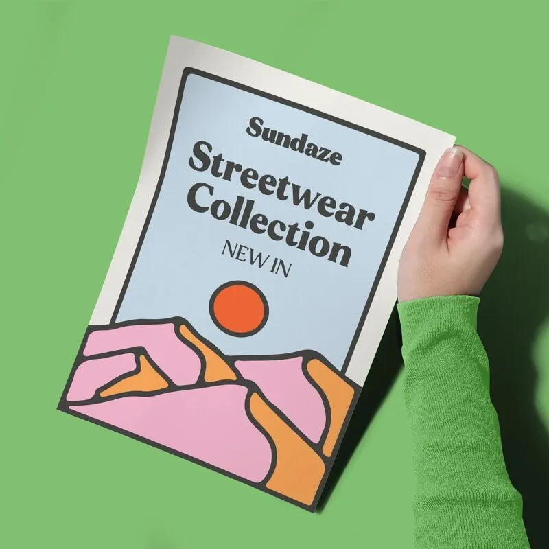 A person's hand holding an A5 Poster for the "Sundaze Streetwear Collection" featuring a colourful, stylised illustration of mountains and a sun.