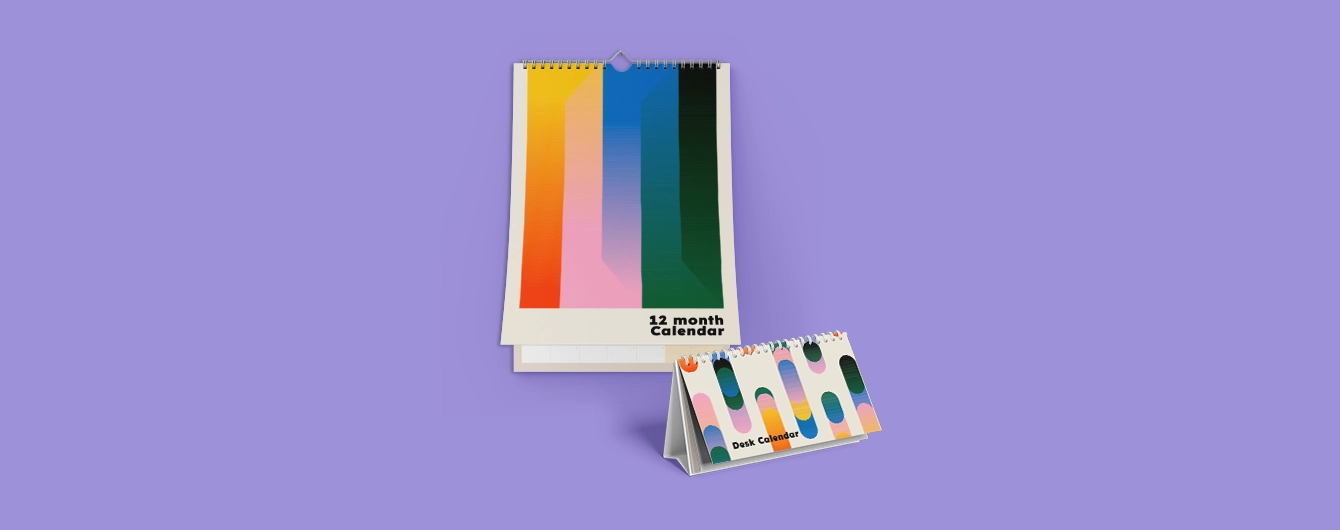 A wire-bound wall calendar reading '12 month Calendar' hanging above a matching standing desk calendar reading 'Desk Calendar', both featuring colourful abstract geometric patterns against a plain purple background.