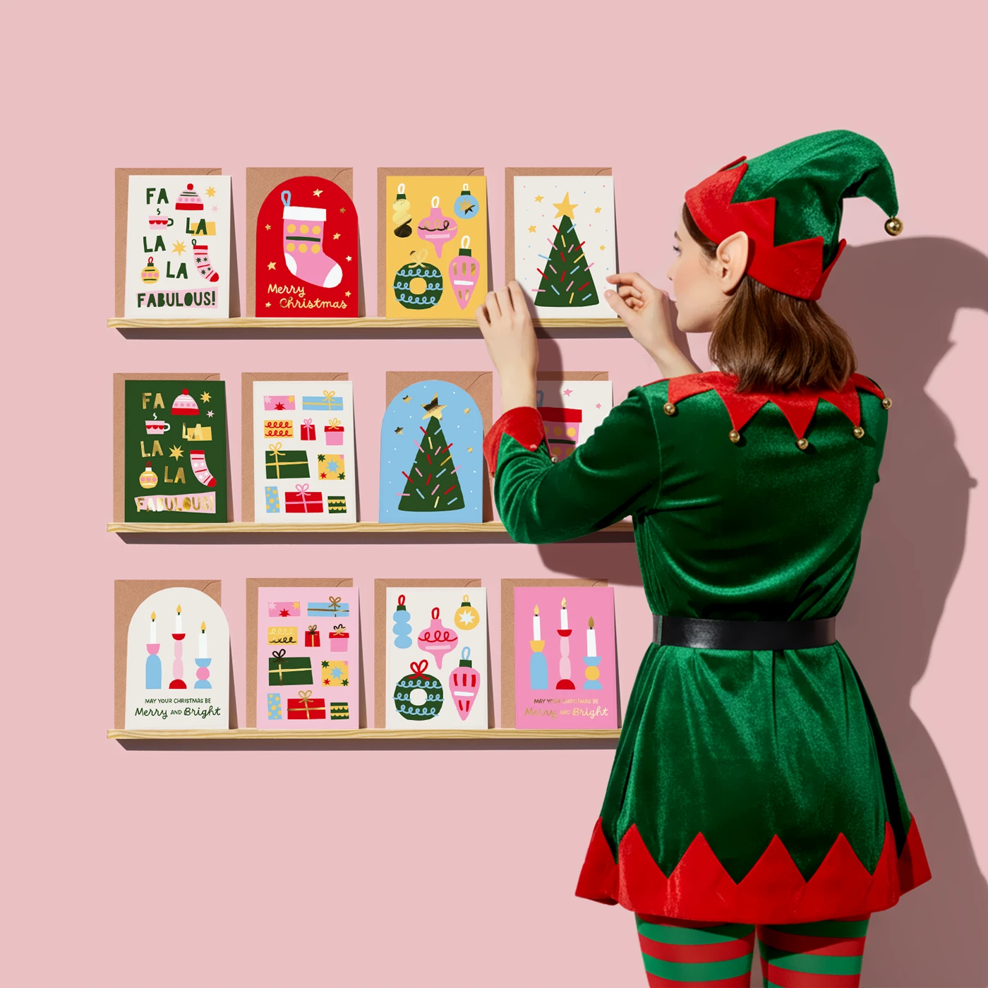 Woman in a green elf costume placing colourful christmas Eco Greeing Cards on wall shelves.