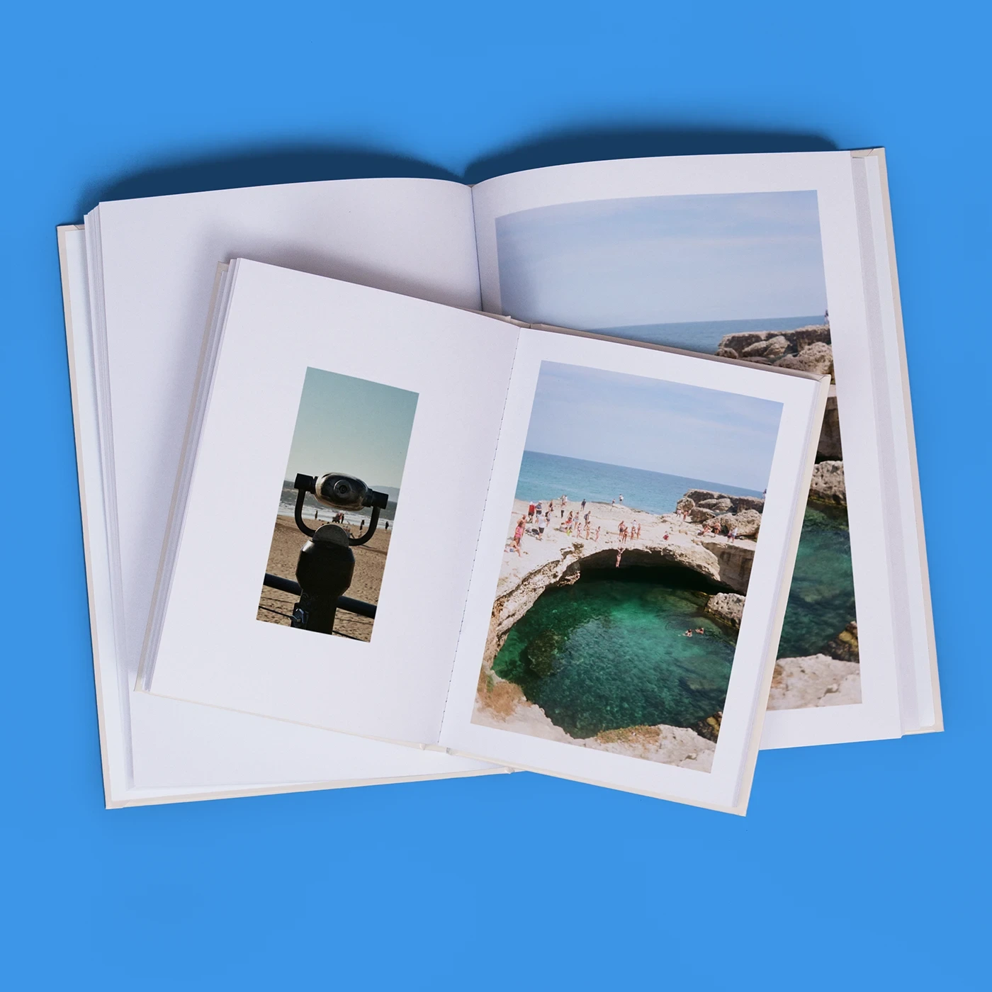 Top-down view of a smaller open Hardback Book displaying photo coastal scenes resting on top of a larger open photo book.