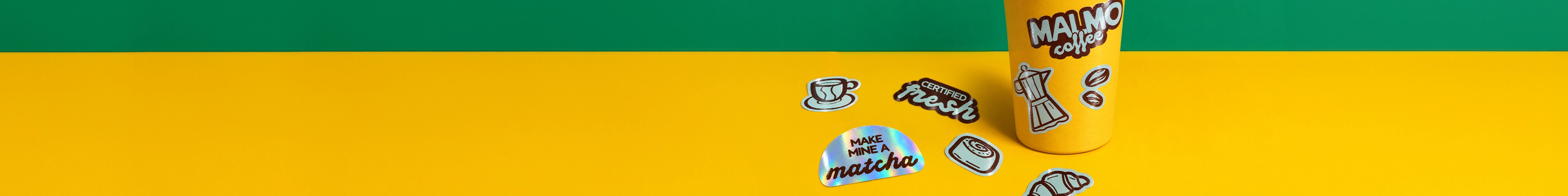 A yellow coffee cup decorated with custom stickers sitting on a bright yellow surface alongside an assortment of coffee-themed die-cut stickers and an arched holographic sticker reading "MAKE MINE A matcha", against a two-tone green and yellow background.
