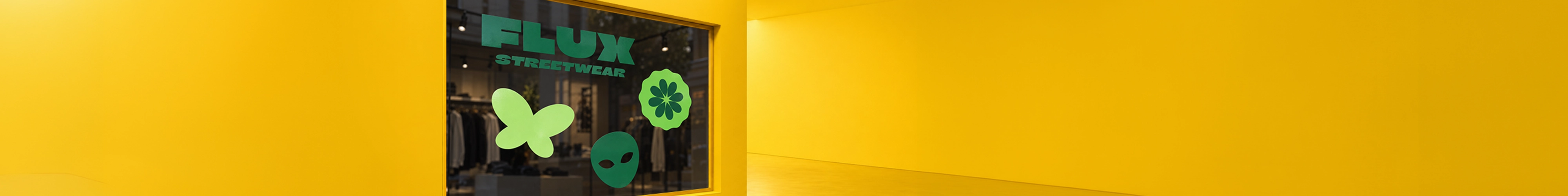 A shopfront window displayed within a bright yellow framed wall, decorated with large green vinyl decals featuring "FLUX STREETWEAR" branding alongside butterfly, flower, and alien shapes.