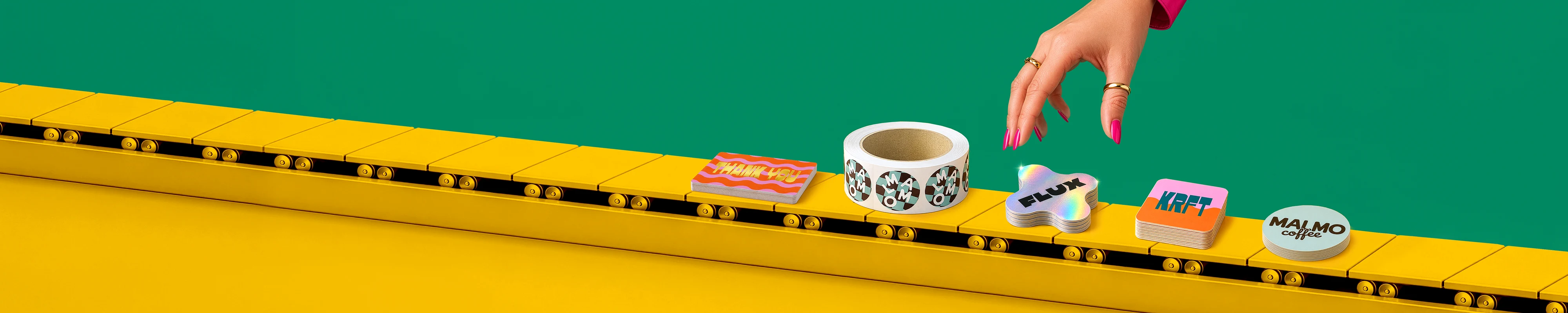 A hand reaches down to select a stack of holographic star-shaped stickers from a yellow conveyor belt displaying an array of colourful custom stickers, labels, and sticker rolls against a vivid green backdrop.