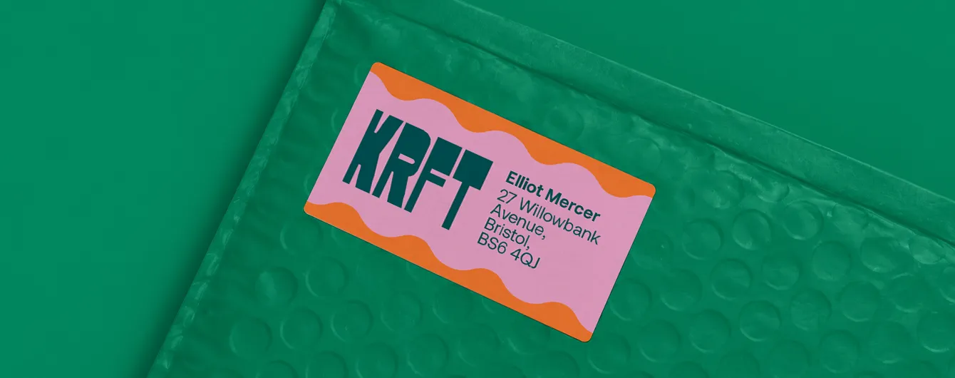 A custom pink and orange wavy-patterned address label printed with the "KRFT" logo and a Bristol recipient address, stuck onto a green padded envelope.
