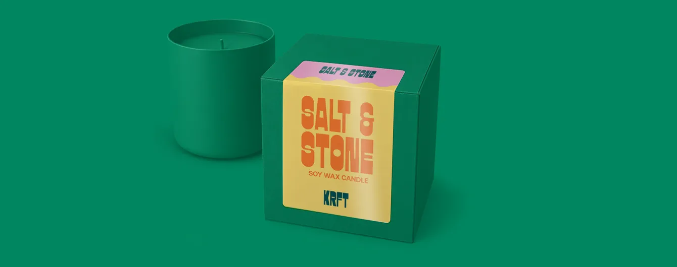 A green candle packaging box featuring a yellow and pink label printed with "SALT & STONE SOY WAX CANDLE KRFT" next to a matching green candle jar.