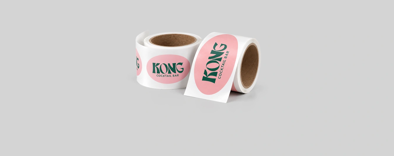 Two rolls of pink Kong Cocktail Bar stickers unrolled on a grey surface