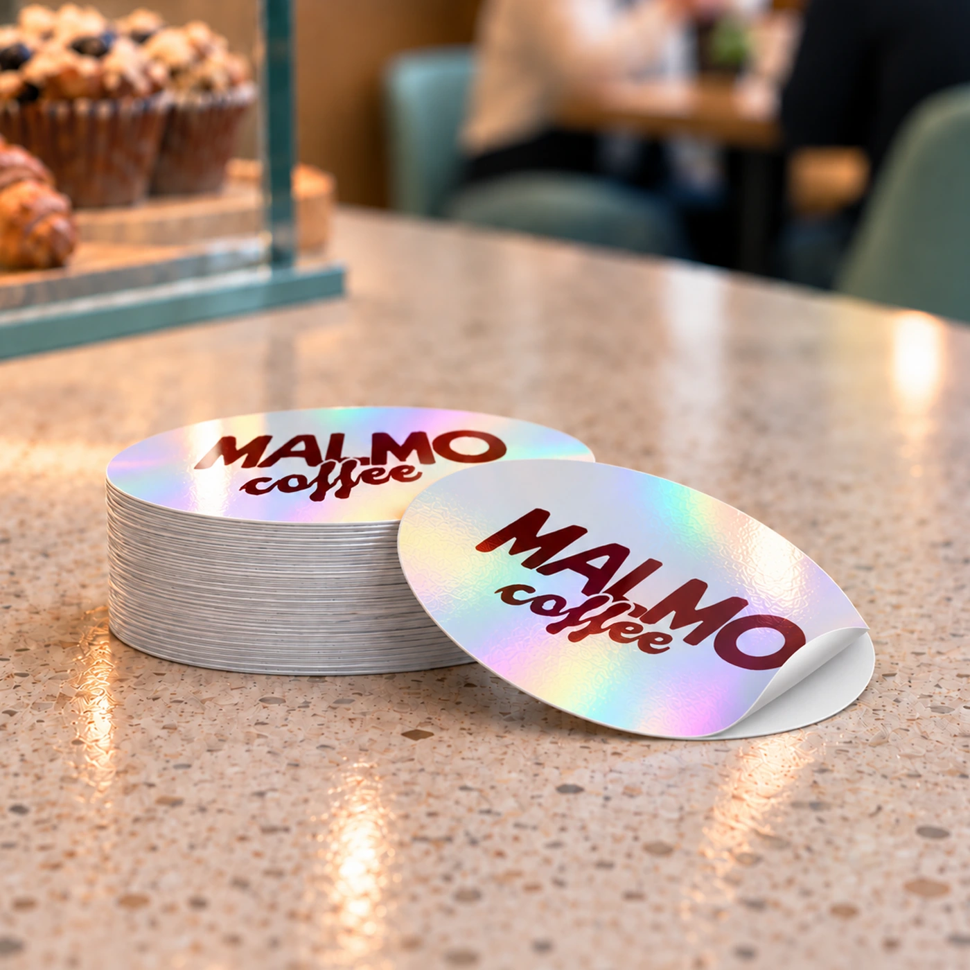 Stack of holographic Malmo Coffee stickers on a cafe counter