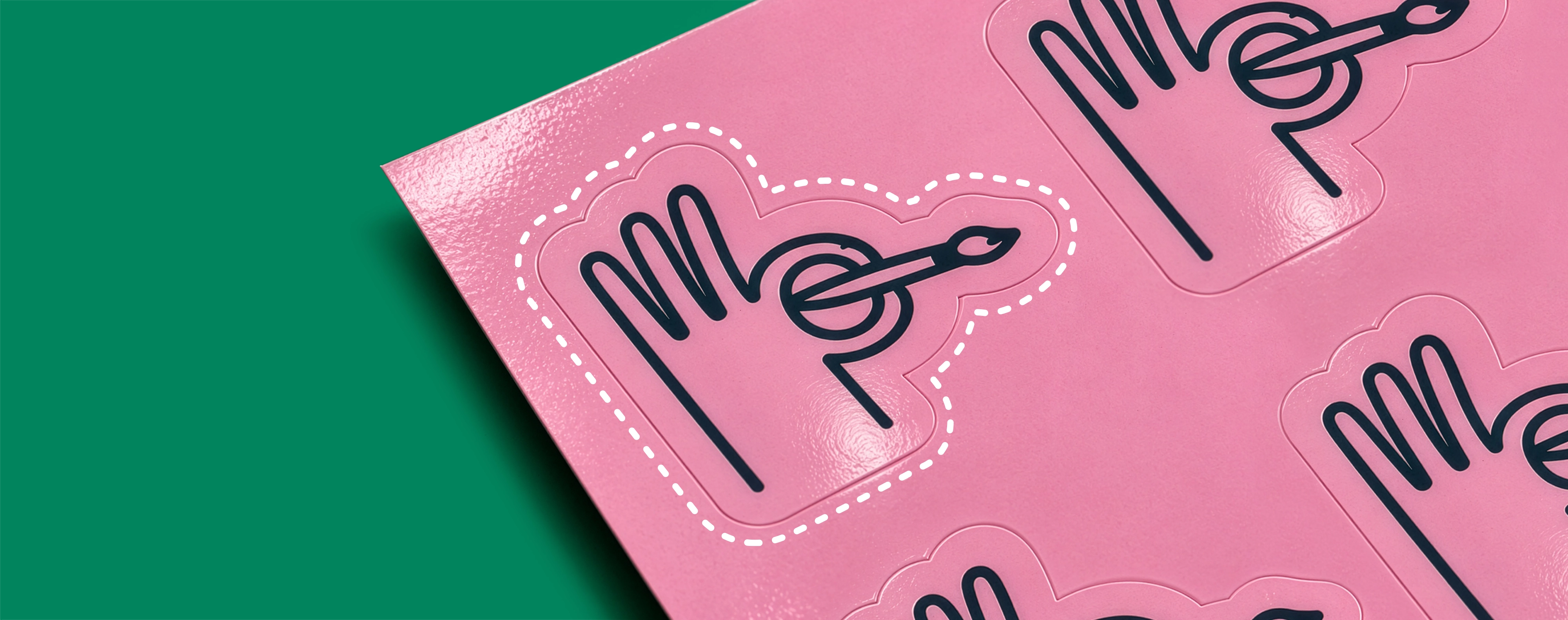 A sheet of pink stickers printed with a hand-and-paintbrush logo, showing a white dashed cut-line around one design.