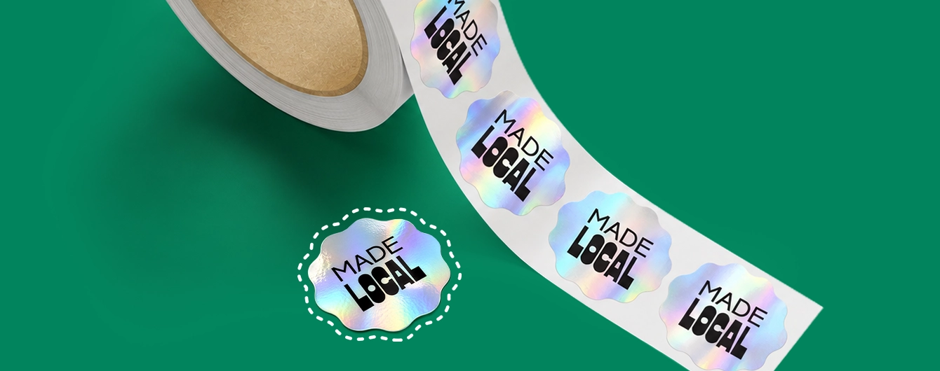 A roll of scalloped holographic stickers reading "MADE LOCAL", with one peel-off sticker highlighted by a white dashed cut-line.
