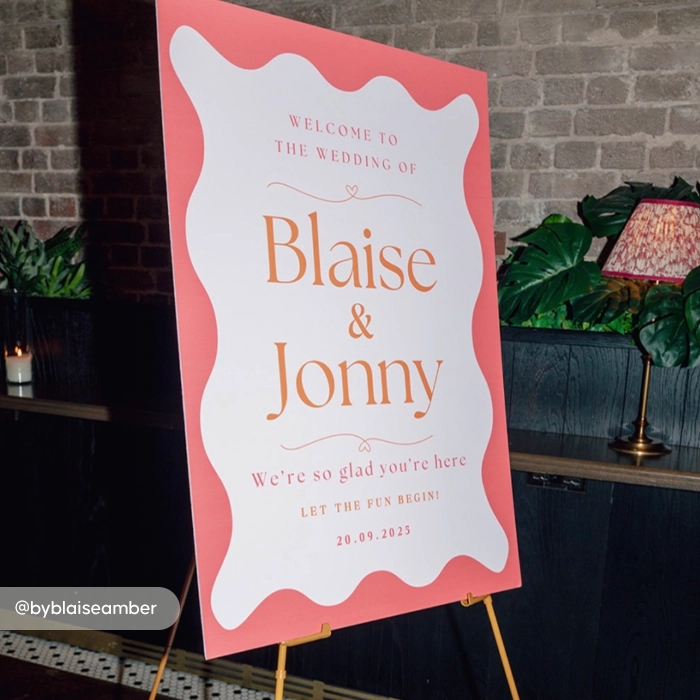 A Wedding Welcome Sign featuring a coral border with a wavy white center reading, "Welcome to the wedding of Blaise & Jonny".