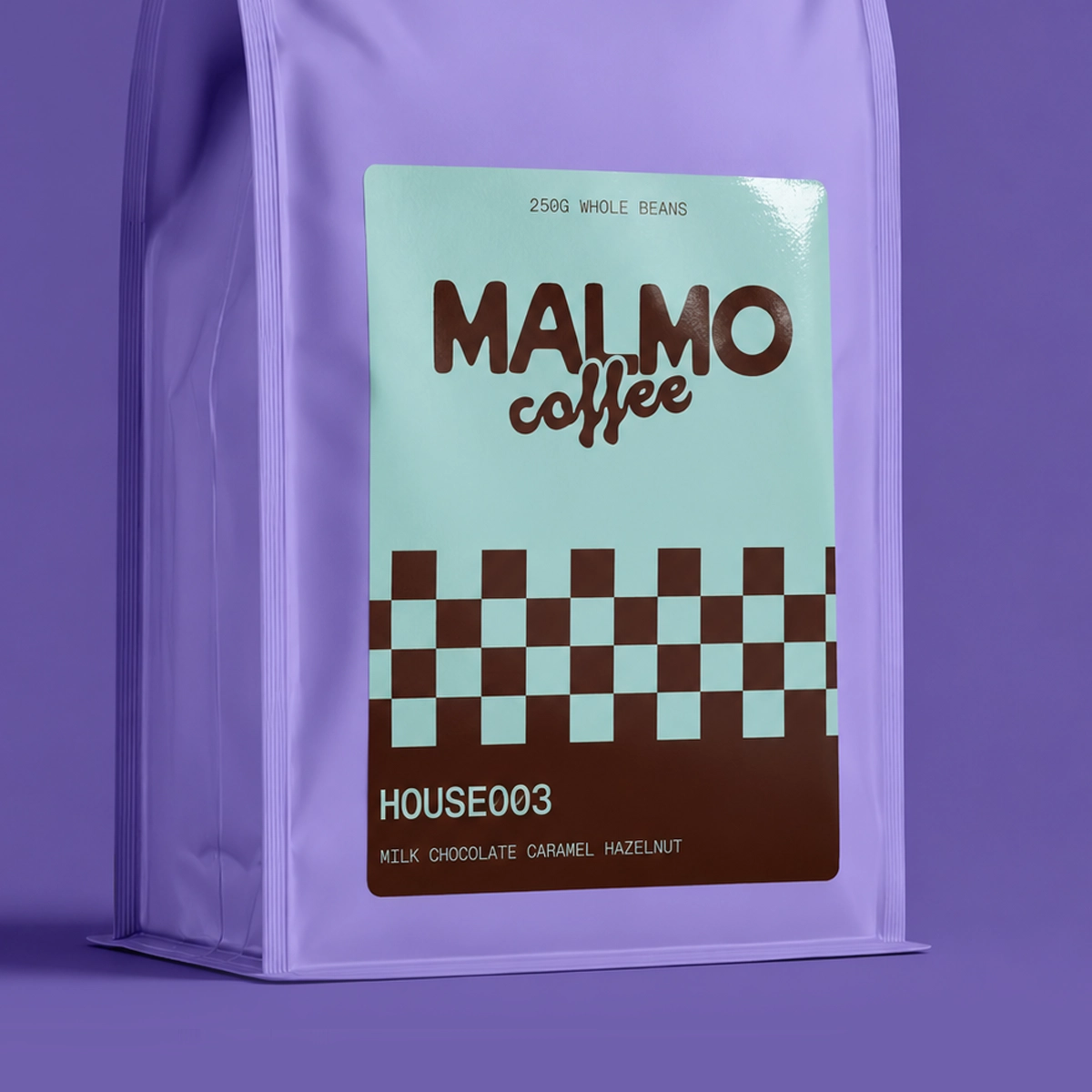 A light-blue branded Food Packaging Label for "Malmo Coffee" whole beans featuring a brown checkered pattern, attached to a coffee bag.