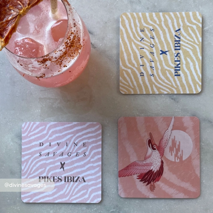 A pink cocktail in a glass beside three patterned Ibiza square Coasters on a marble surface, featuring zebra prints.
