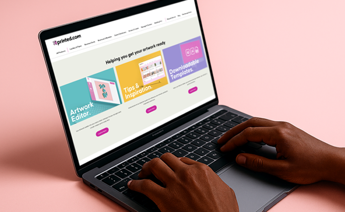 A person using a laptop displaying the printed.com homepage with options for Artwork Editor, Tips & Inspiration, and Downloadable Templates.