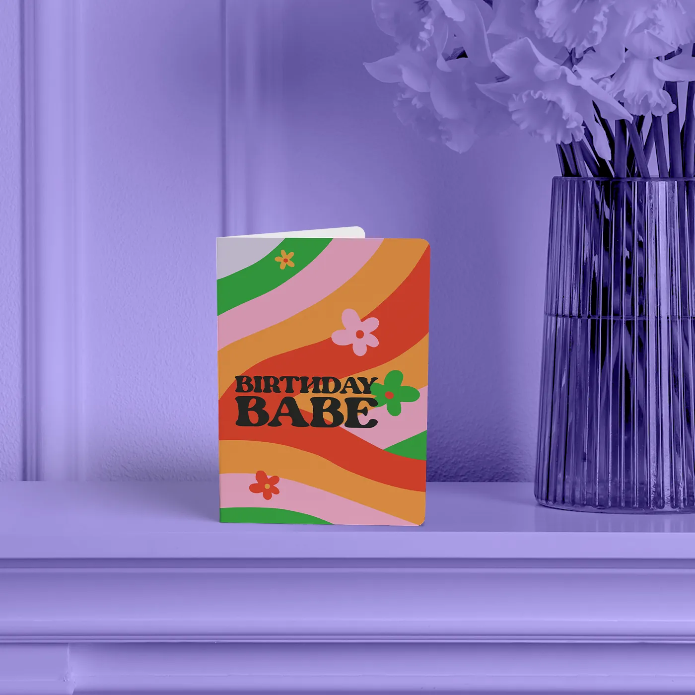 Retro-style "Birthday Babe" Greeting Card with round corners, featuring colourful wavy stripes and flower doodles, displayed on a shelf next to a vase.