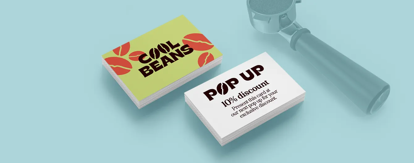 Two stacks of Cool Beans branded business cards resting on a light blue surface alongside a coffee machine portafilter, displaying "10% discount" promotional details.