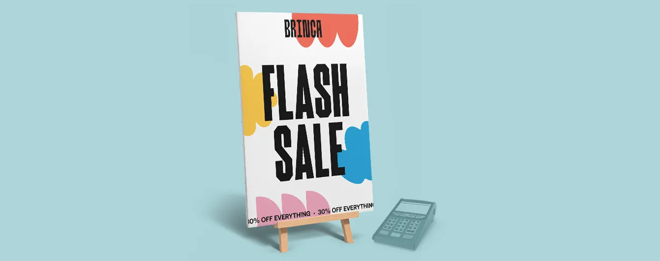 A desktop promotional sign reading "BRINCA FLASH SALE - 30% OFF EVERYTHING" displayed on a small wooden easel beside a card reader on a light blue background.