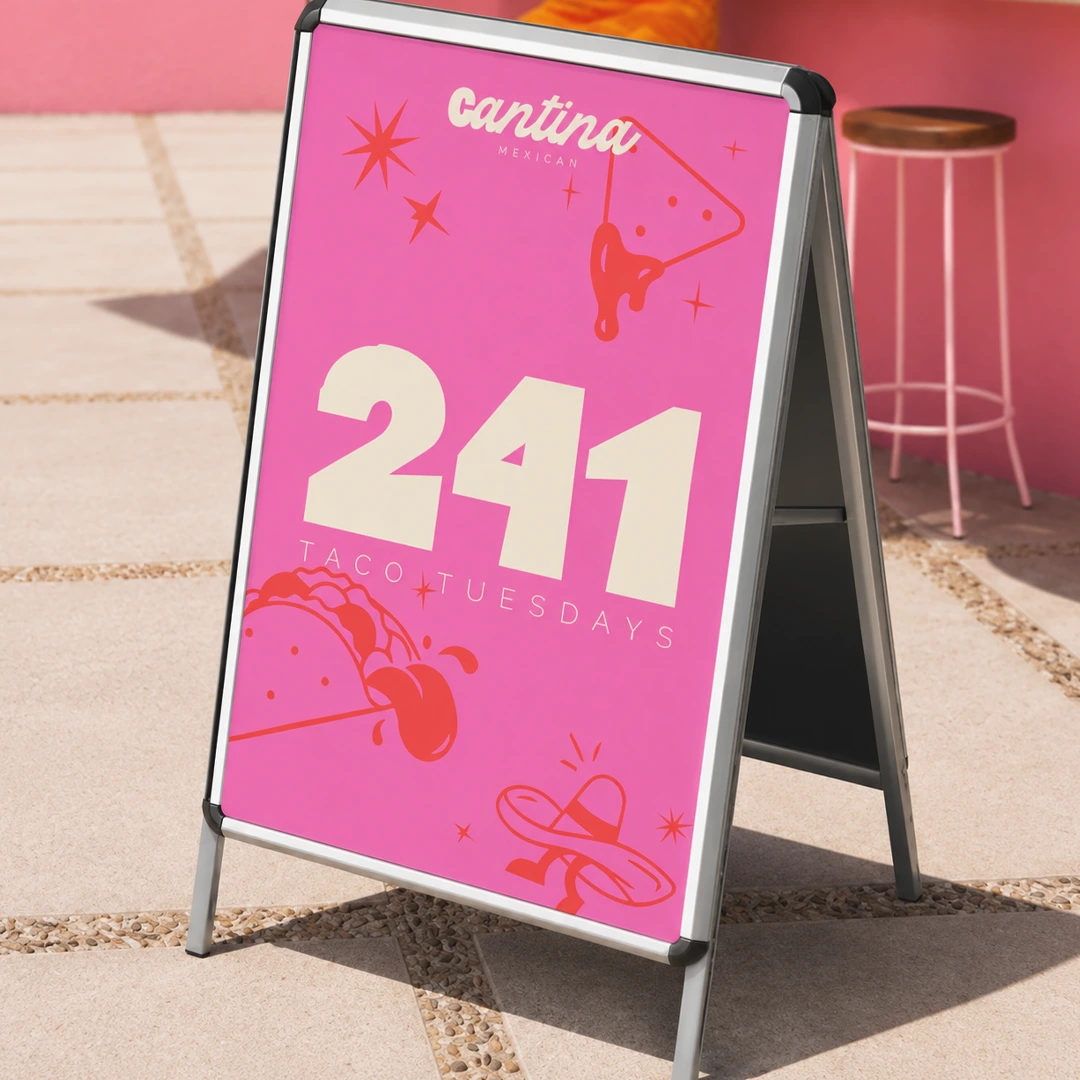A silver pavement Outdoor Menu Board with a-board hardware featuring a bright pink "Cantina" poster advertising "241 Taco Tuesdays" with festive Mexican food illustrations.