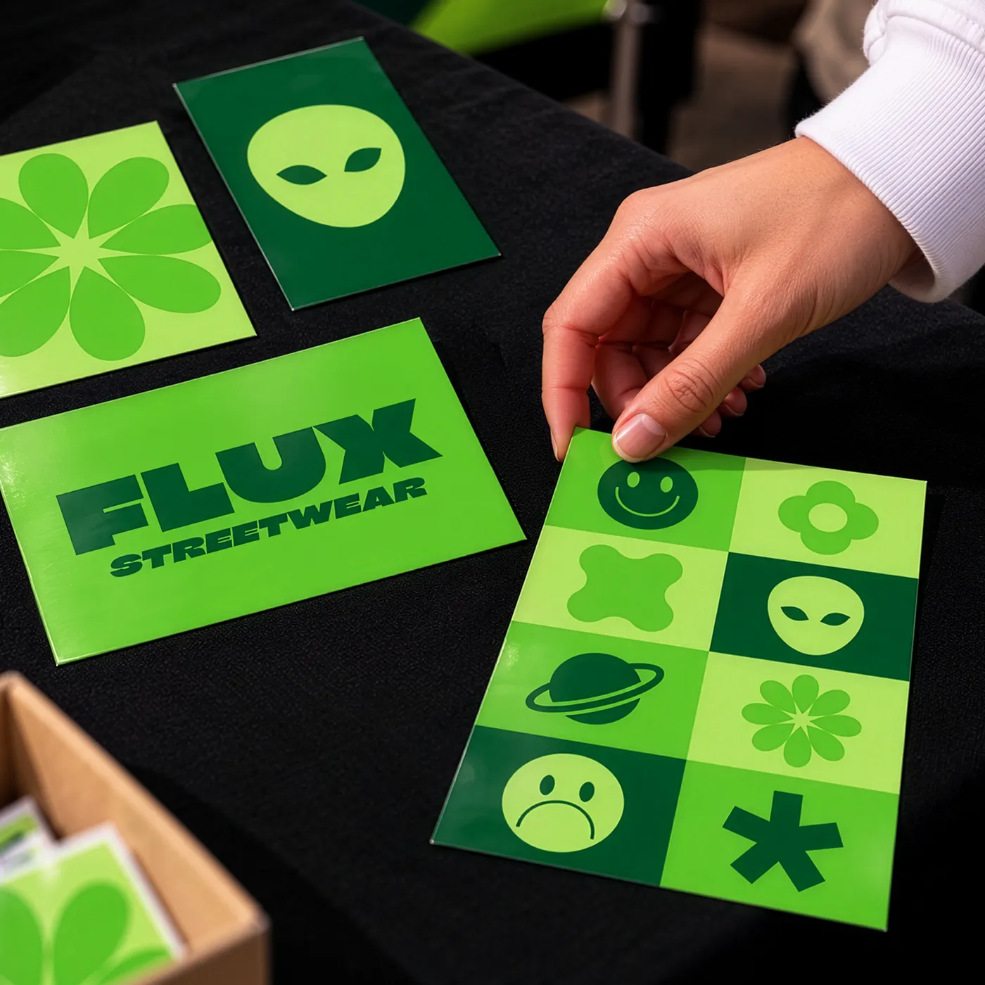 A person holding green A-Size streetwear Stickers, including an alien graphic and a FLUX Streetwear print.