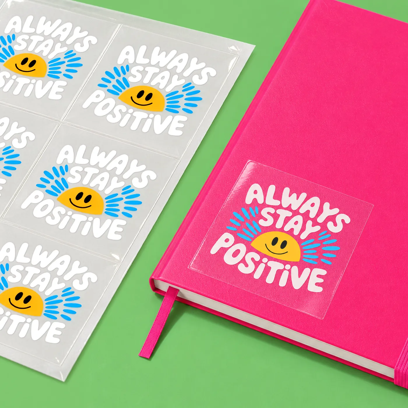 Clear Sticker Sheets with "Always stay positive" messaging, wit one Sticker on a notebook.