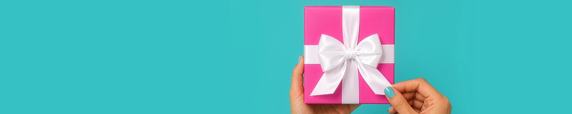 Two hands hold a bright pink gift box tied with a white satin ribbon against a teal background, with one hand gently pulling the ribbon's end.