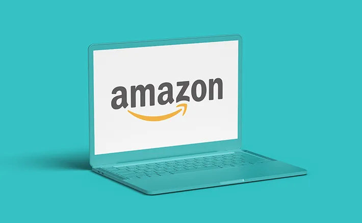 A teal laptop set against a matching teal background, displaying the Amazon logo on its screen.