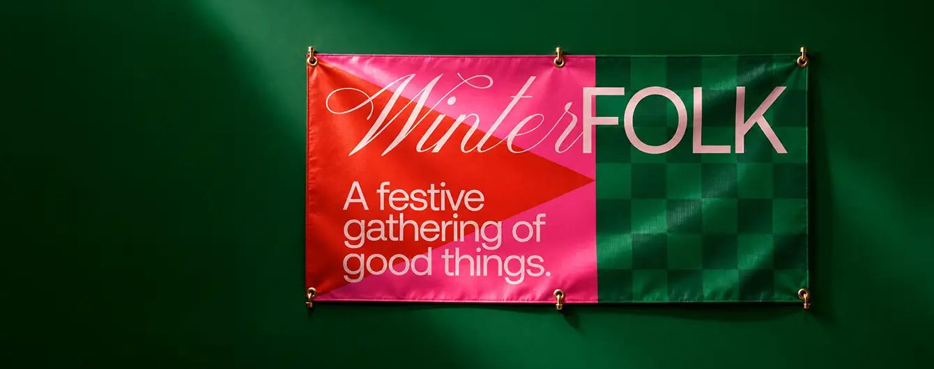 A colouful "Winter FOLK: A festive gathering of good things." hanging Banner displayed against a dark green backdrop