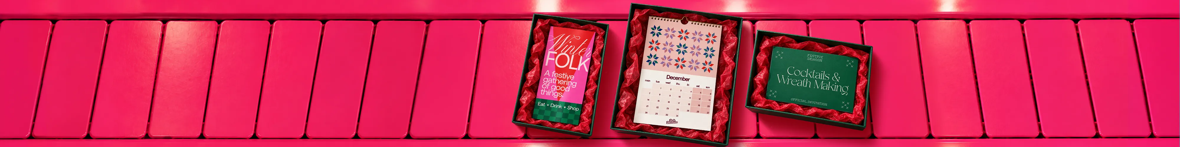 An open gift box lined with red tissue paper contains a pink 'Winter Folk' leaflet on the left and a December calendar with geometric patterns on the right, set against a bright pink surface.