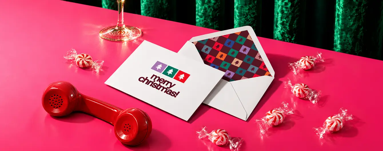 A white "Merry Christmas" card next to an open white Envelope with a patterned Envelope Liner, displayed on a pink surface with a red telephone handset and peppermint candies