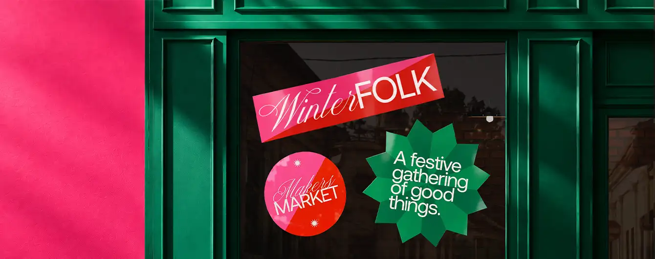 A dark green storefront window styled with colourful festive Vinyl Decals reading "Winter FOLK", "WINTER MARKET", and "A festive gathering of good things".