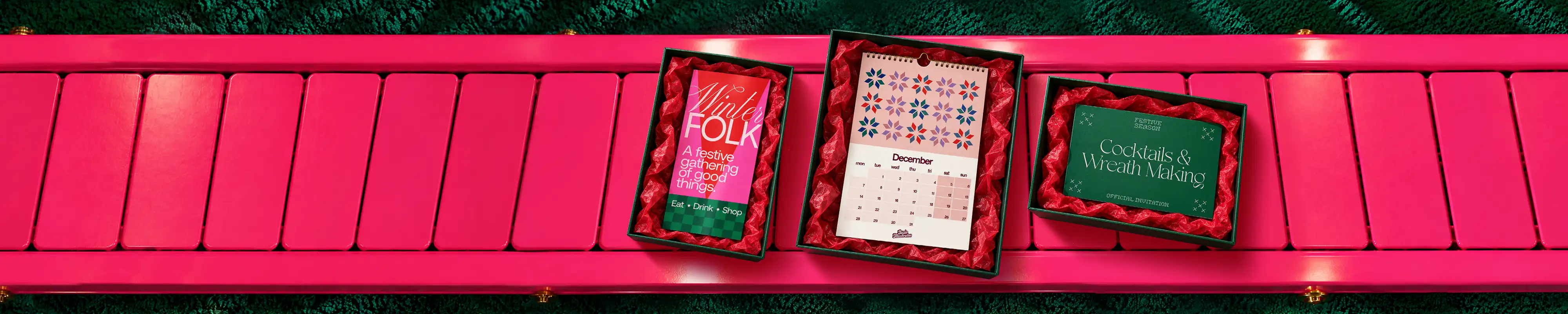 Christmas-themed gifts and products on a bright pink wooden backdrop with festive lights.